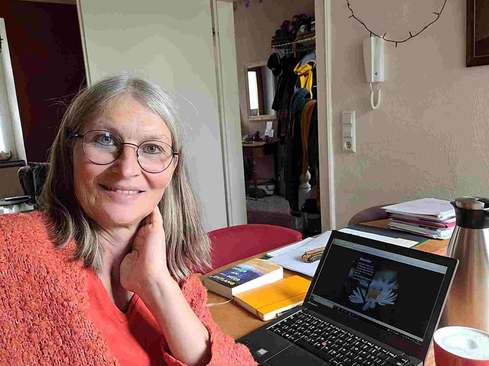 Selfie einer Frau mit halblangen Haaren am Laptop, der auf einem Esstisch steht