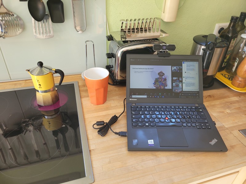 Laptop mit einer laufenden Online-Präsentation neben einem Herd mit Bialetti-Espressokocher