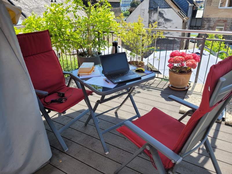 Balkon mit zwei Stühlen und einem Tisch, auf dem ein Laptop aufgeklappt ist.
