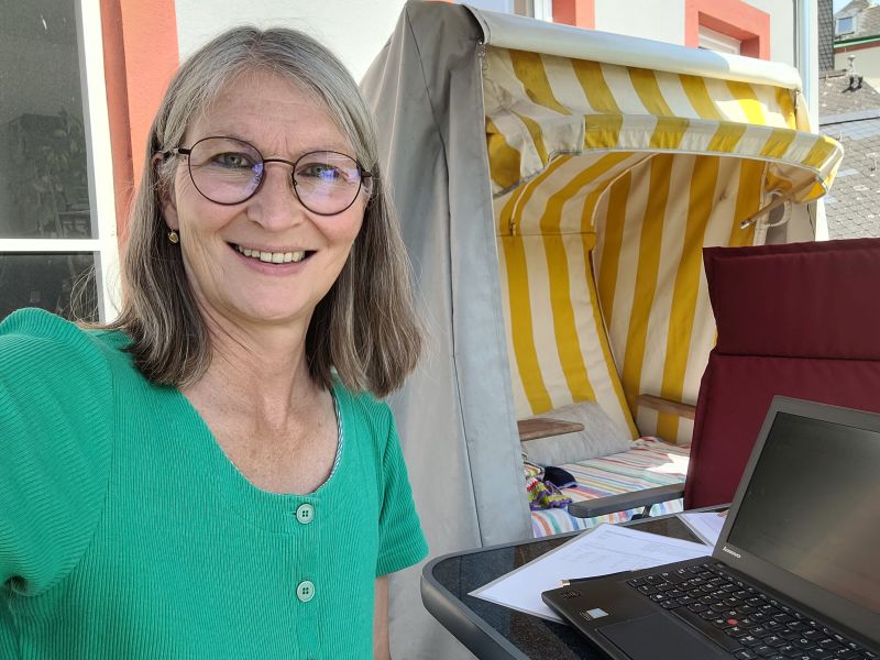 Selfie von Gabi Kremeskötter auf ihrem Balkon, im Hintergrund ein gelb-weißer Strandkorb