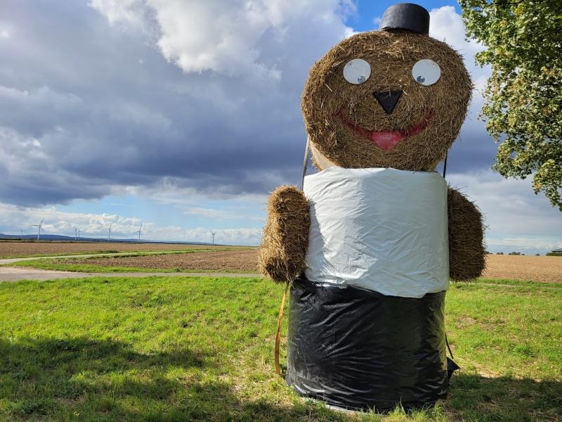 Ein Mann aus großen Strohballen grüßt am Wegesrand.