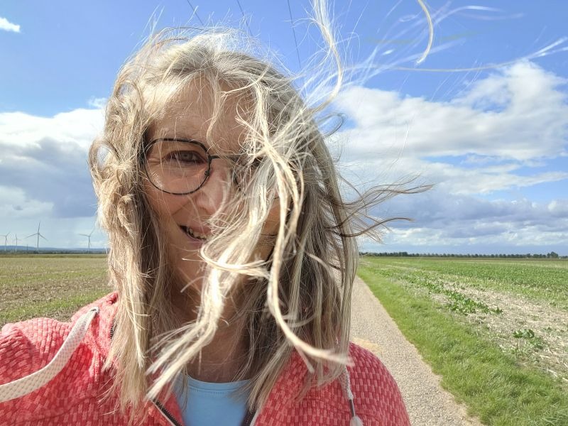 Frau mit vom Wind verwehten Haaren vor blauem Himmel.