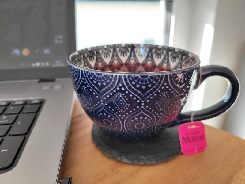 Eine große Teetasse mit Teebeutel, daneben der Rand eines Laptops.