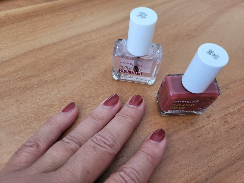 Frauenhand mit rot lackierten Fingernägeln, daneben die Fläschchen mit Lack und Überlack.