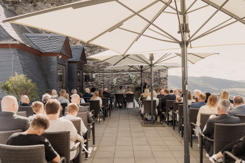 Freie Trauung auf einer Dachterrasse, Rückansicht der Gäste in Stuhlreihen unter großen Sonnenschirmen, im Hintergrund das Brautpaar und die Freie Rednerin