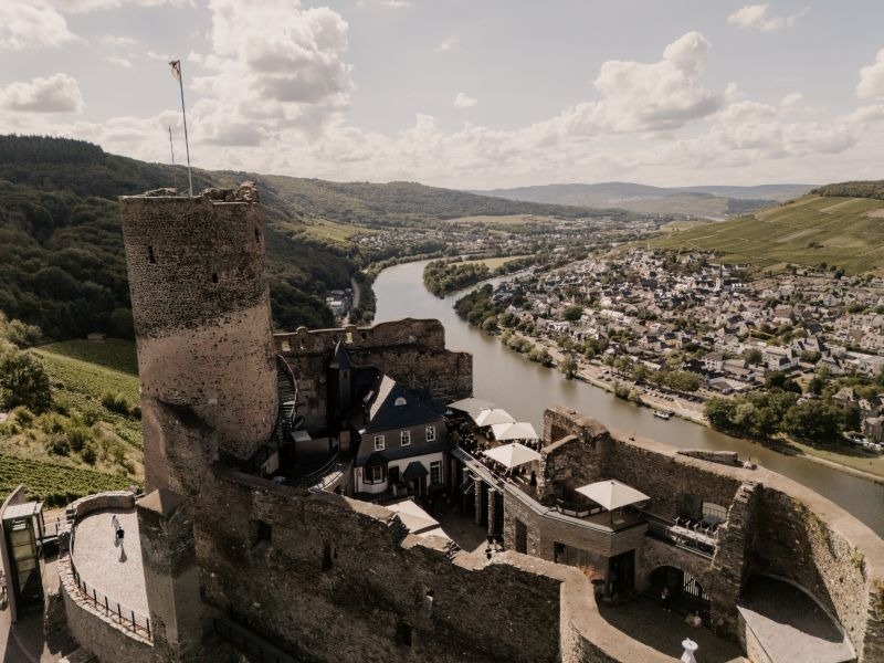 Burg Landshut in Bernkastel-Kues, Drohnenaufnahme, von oben zu sehen die Dachterrasse, der Innenhof und Turm, im Hintergrund die Mosel und Stadtteil Kues