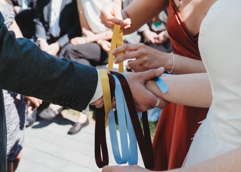 Wrap Handfasting Anleitung Schritt 4: Das 3. und 4. Band des WRAPs wird gelegt von den Trauzeug:innen um die Hände gewickelt.