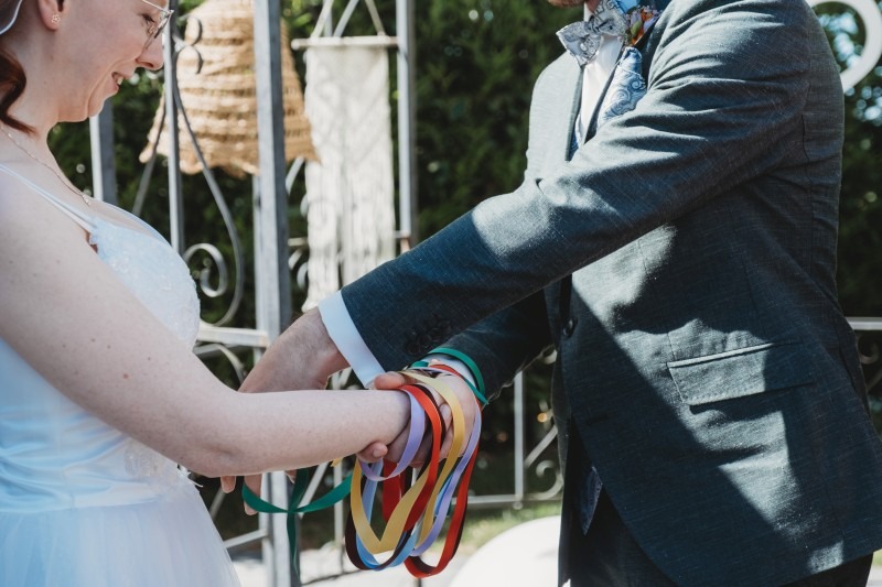 Wrap Handfasting Anleitung Schritt 5: Der Bräutigam wickelt sein Band um die gehaltenen rechten Hände, bis 6 bunte Bänder ihre Hände fast verstecken.