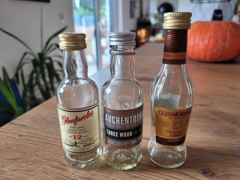 Drei leere Probeflaschen verschiedener Whiskys: Glenfarclas, Auchentoshoan, Glenmorangie