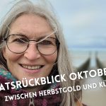 Frau mit Wind in den Haaren schaut in die Kamera, im Hintergrund das Meer und Strand mit Poldern.