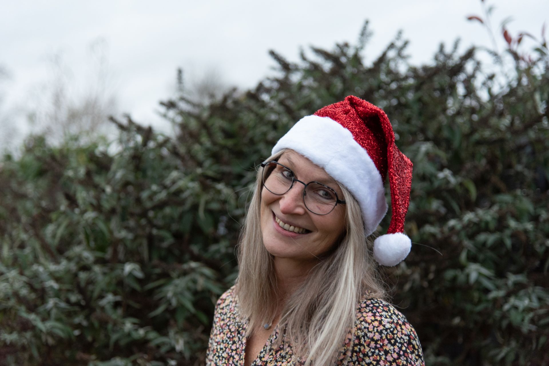 Frau (Gabi Kremeskötter) mit grau-blonden langen Haaren ,vor grüner Hecke mit Nikolausmütze