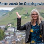 Gabi Kremeskötter steht mit erhobenen Händen vor den Weinbergen an der Mosel, ihre Hände bilden eine Waage, darüber der Text: "Mein Motto 2026: Im Gleichgewicht sein"