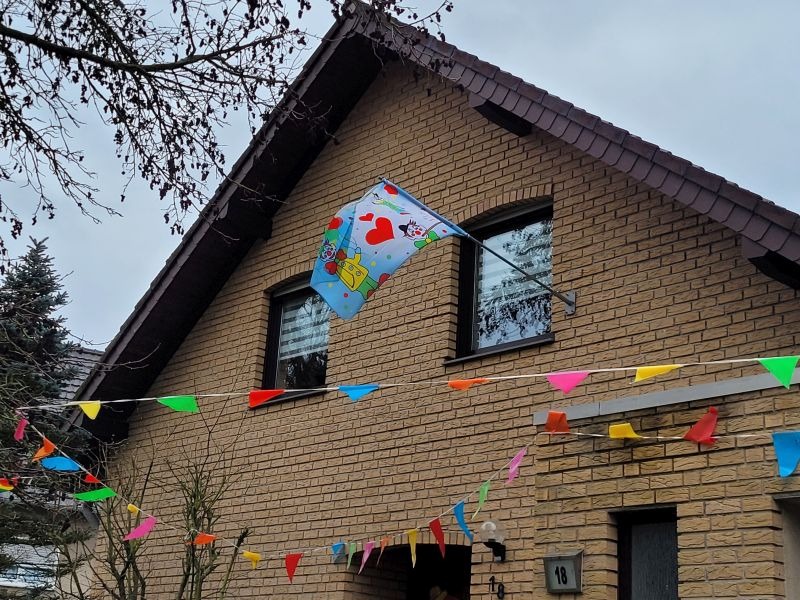 Bunte Fähnchen und eine Karnevalsflagge vor einem Haus.