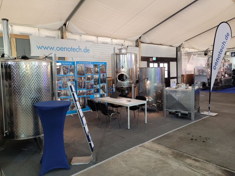 Messestand Oenotech.de mit aufgebauten Edelstahltanks und Roll-Ups, in der Mitte ein Tisch mit Stühlen und Laptop