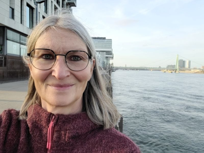 Selfie einer Frau am Rhein, im Hintergrund der Fluss und etwas verborgen die Kranhäuser