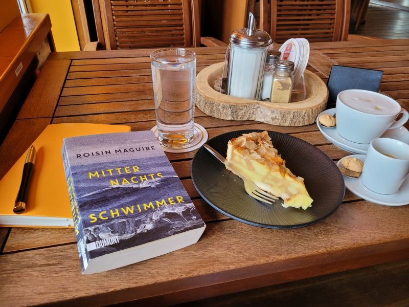 Roman Mitternachtsschwimmer von Roisin Maguire auf einem Tisch bei Kaffee und Kuchen
