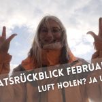 Langhaarige, lächelnde Frau in Winterjacke mit hoch hochgehaltenen Händen und abgespreitzten Fingern vor wolkigem Himmel.