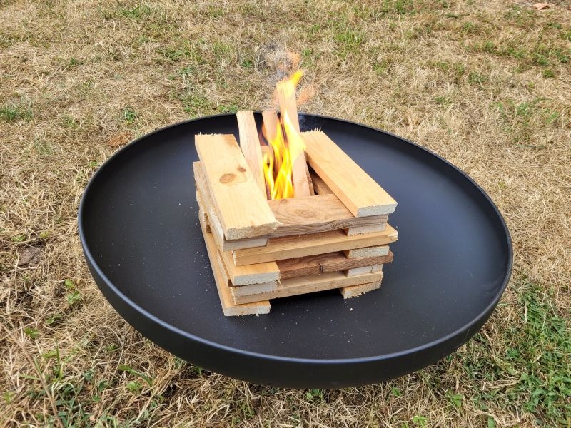 Eine schwarze Feuerschale mit geschichtetem, brennenden Holz