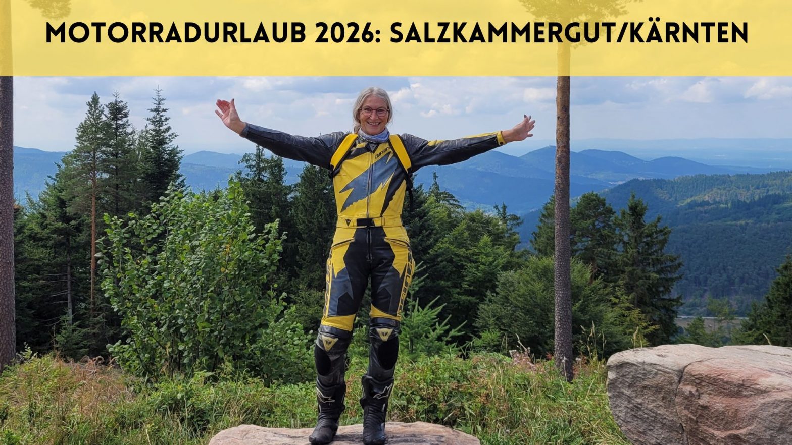 Frau steht in gelbschwarzer Motorradkombi mit ausgebreiteten Armen vor Panorama im Nordschwarzwald. Darüber der Text: Motorradurlaub 2026: Salzkammergut/Kärnten