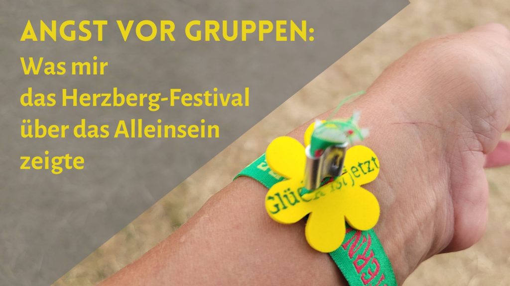 Arm mit Bändchen des Herzberg-Festivals 2026 und Blume "Glück ist jetzt", daneben der Schriftzug: "Angst vor Gruppen: Was mir das Herzberg-Festival über das Alleinsein zeigte"