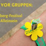 Arm mit Bändchen des Herzberg-Festivals 2026 und Blume "Glück ist jetzt", daneben der Schriftzug: "Angst vor Gruppen: Was mir das Herzberg-Festival über das Alleinsein zeigte"