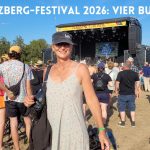 Frau mit Kappe vor der Hauptbühne des Herzberg-Festivals 2026; darüber der Text: Mein Herzberg-Festival: Vier bunte Tage