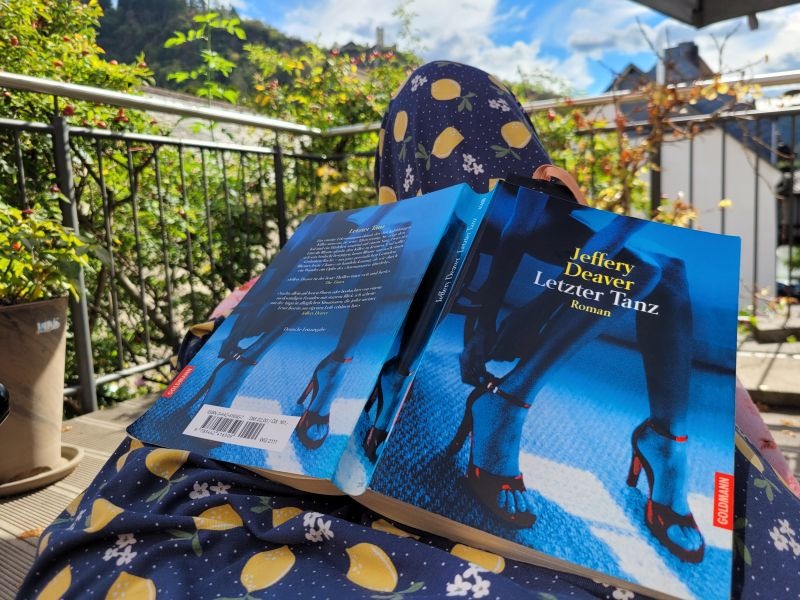 Buch von Jeffrey Deaver Letzter Tanz liegt mit dem Einschlag nach oben auf den Knien eines bunten Sommerkleides