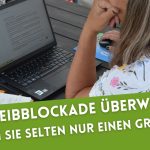 Rückansicht einer Frau, die am Laptop arbeitet, neben sich ein Notizbuch