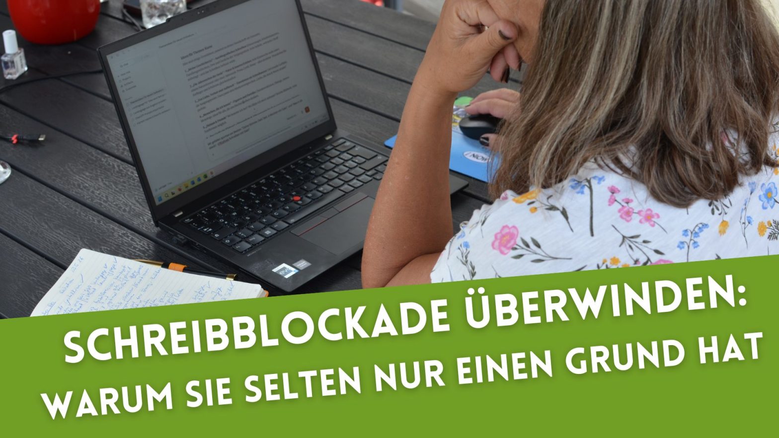 Rückansicht einer Frau, die am Laptop arbeitet, neben sich ein Notizbuch